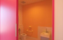 通路から見るトイレ内部　ピンク色の扉　黄色の壁